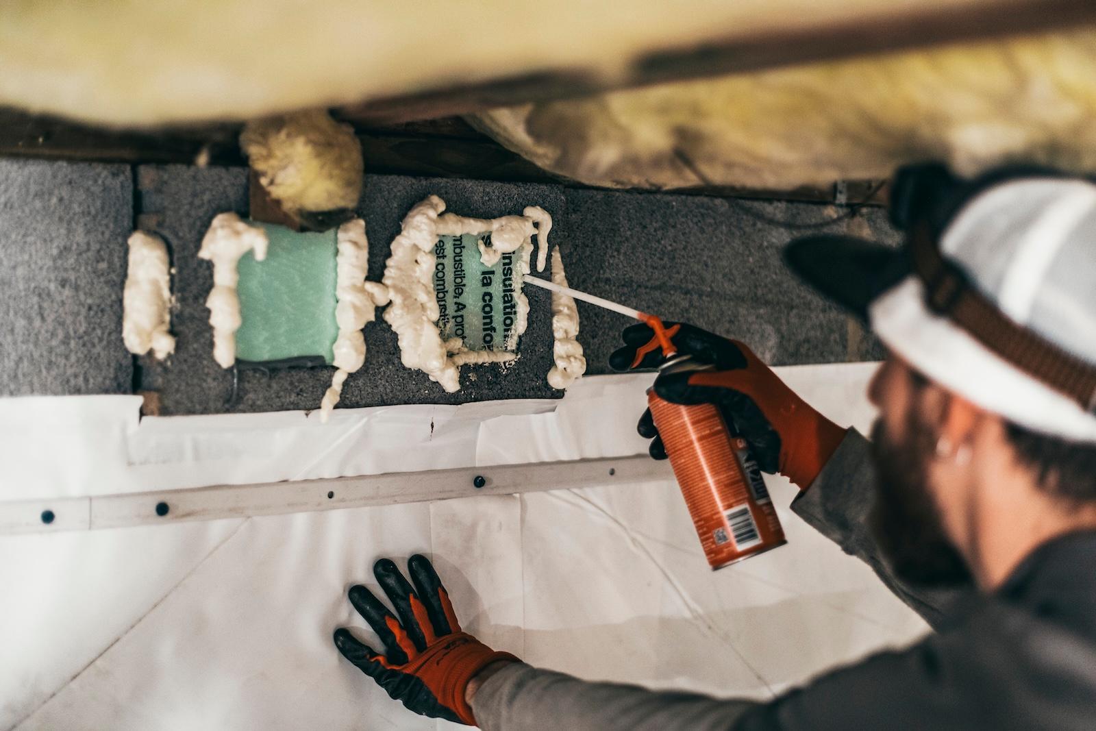 A Crawlspace Medic installer applying closed-cell spray foam to a crawl space perimeter wall