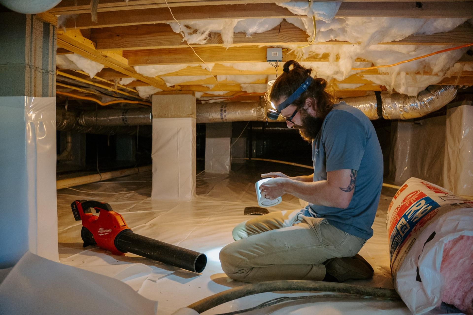 A Crawlspace Medic technician laying vapor barrier under a home