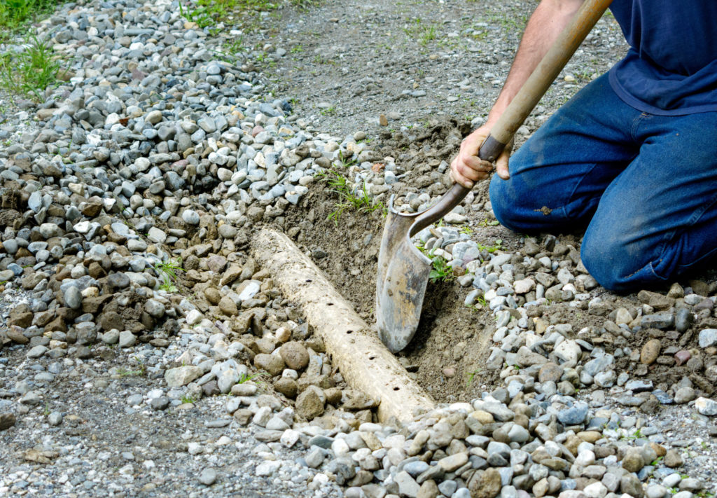 Man digging out french drain in driveway to clean out